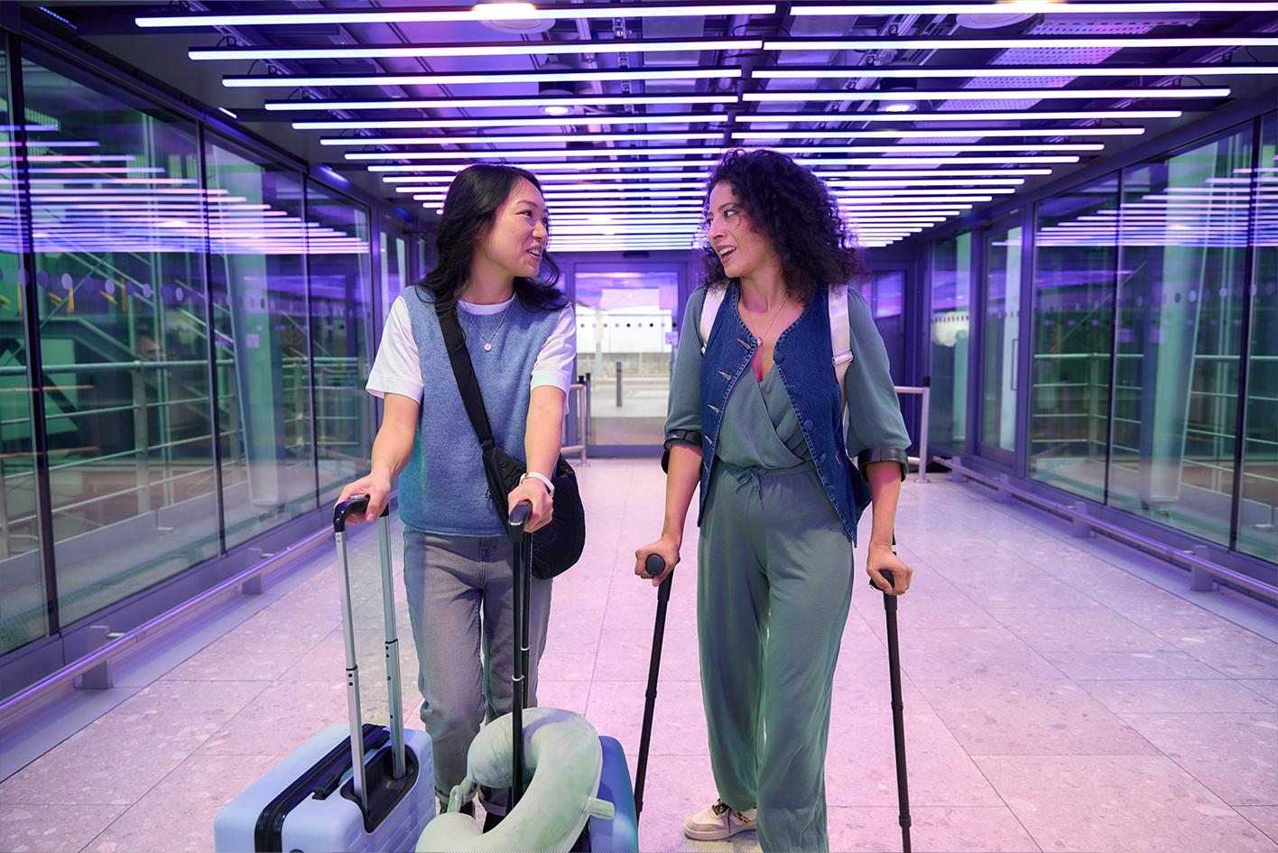 Two women walking through the airport, the woman on the right is using crutches.