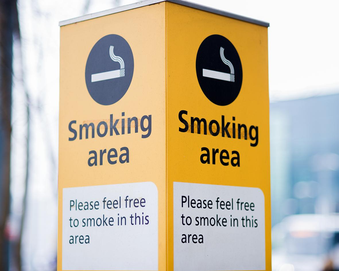 Image of yellow smoking area sign that says smoking area with an image of a cigarette and a box that says please feel free to smoke in this area